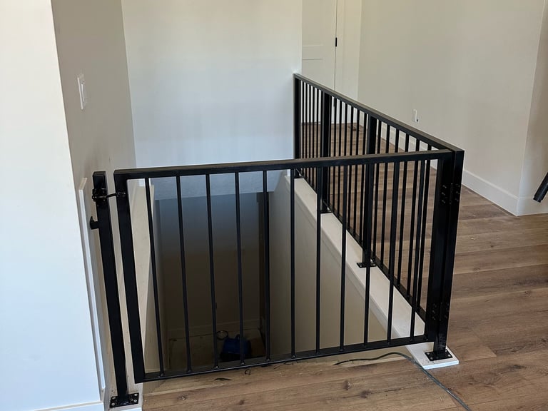 Black metal baby gate installed at top of staircase in hallway with white walls