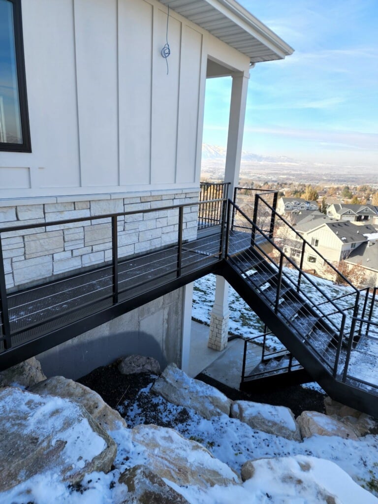 Modern white house with metal railing deck overlooking snowy rocky terrain and city valley landscape
