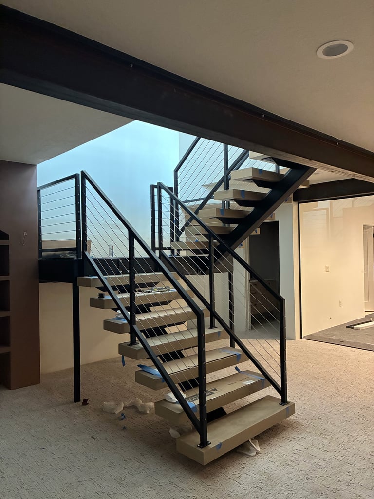 Modern staircase with black metal railings and cable detailing in an open interior space with concrete flooring and high ceilings