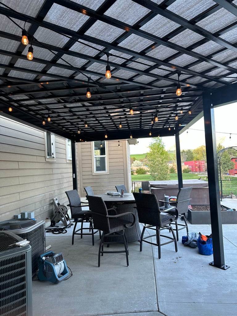 Modern black pergola with hanging lights over a patio seating area with bar-height chairs and an air conditioning unit