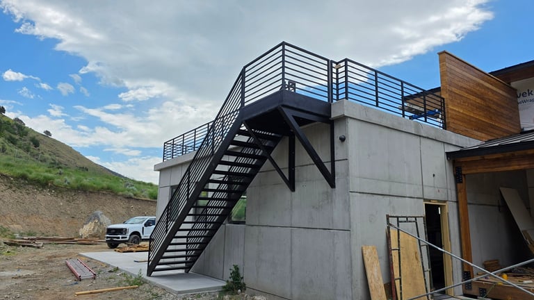 Industrial concrete structure with external black metal staircase and rooftop deck in mountainous terrain