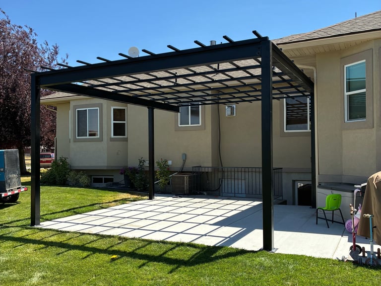 Modern black metal pergola attached to tan house with patterned patio and green lawn