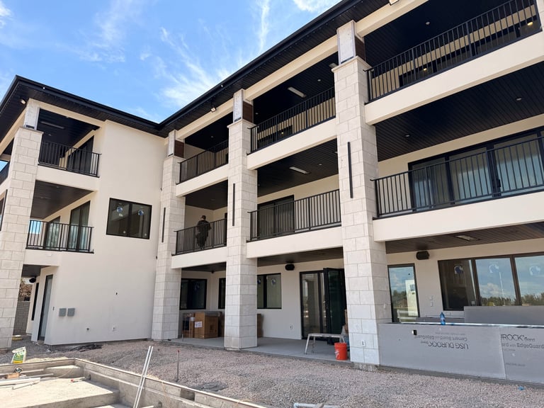 Modern white apartment building with multiple balconies, concrete columns, and ground-level retail spaces under construction
