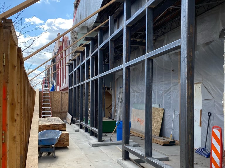 Construction site with metal scaffolding, plastic sheeting, and materials along a brick building exterior during daytime