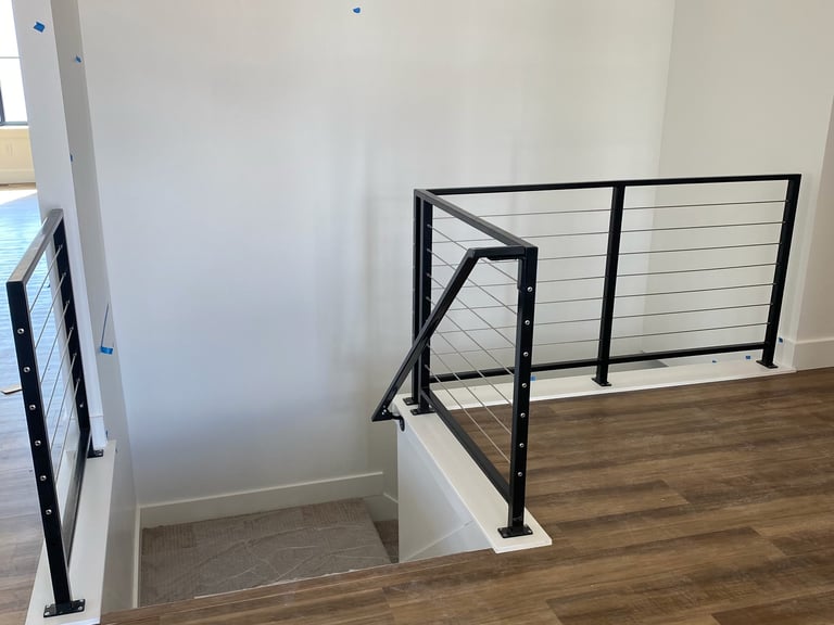 Modern staircase with black metal cable railings and white newel posts on wooden flooring
