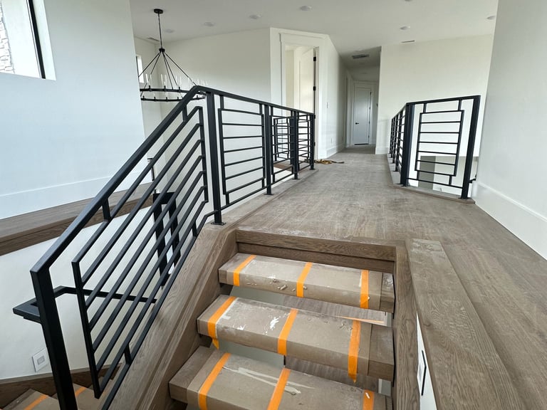 Modern hallway with black metal stair railing, rolled flooring materials wrapped in orange straps, and white walls with pendant lighting