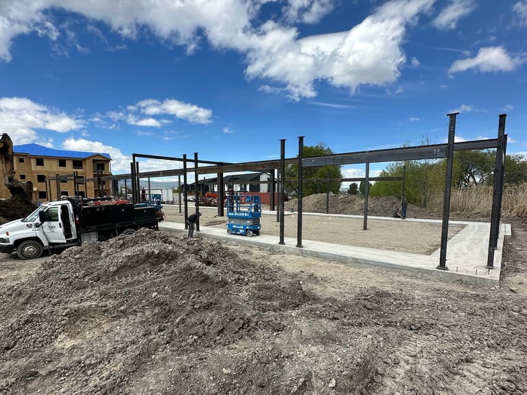 Construction site with steel frame structure, white truck, yellow building, and desert landscape under blue sky
