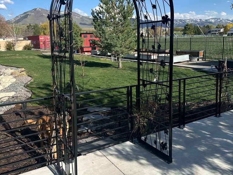 Black metal garden arbor gateway on concrete patio with rural property and mountains in background