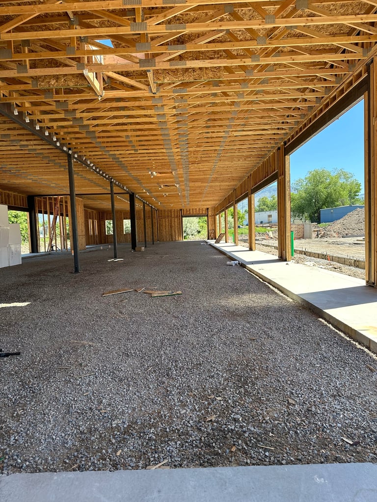 Interior of a wooden-framed covered structure under construction with gravel floor and open sides overlooking landscaping