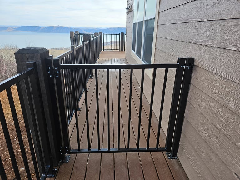 Black metal safety gate on a wooden deck with lake and mountains visible in the background