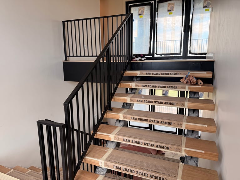 Indoor staircase with wooden steps and black metal railings, with safety warning labels on each step and windows visible at the top landing.