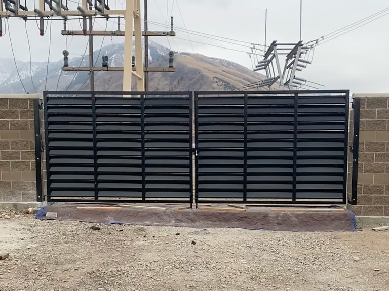 Large black horizontal slat driveway gate installed between brick pillars with mountains visible in background