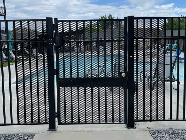 Black metal gate at pool entrance with blue water and loungers visible beyond the fence