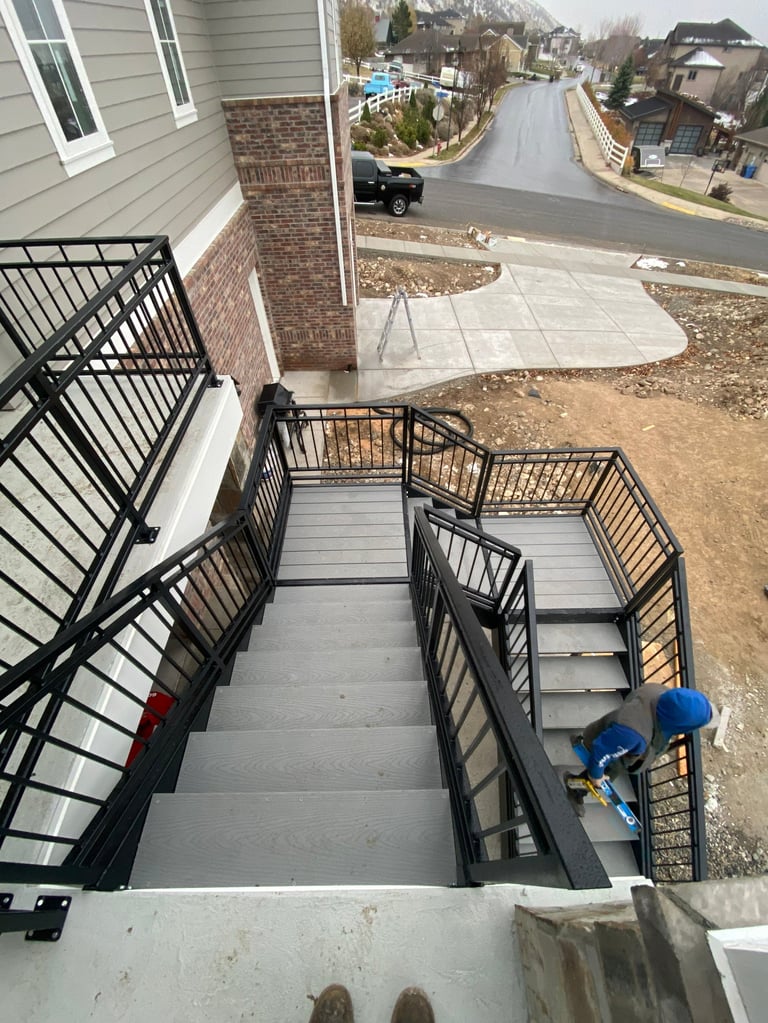 Overhead view of metal staircase with black railings leading down to a concrete patio and suburban street