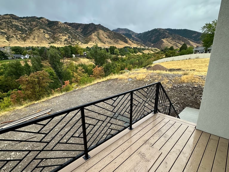 Modern deck with geometric black metal railing overlooking dry hills, green valley, and mountains