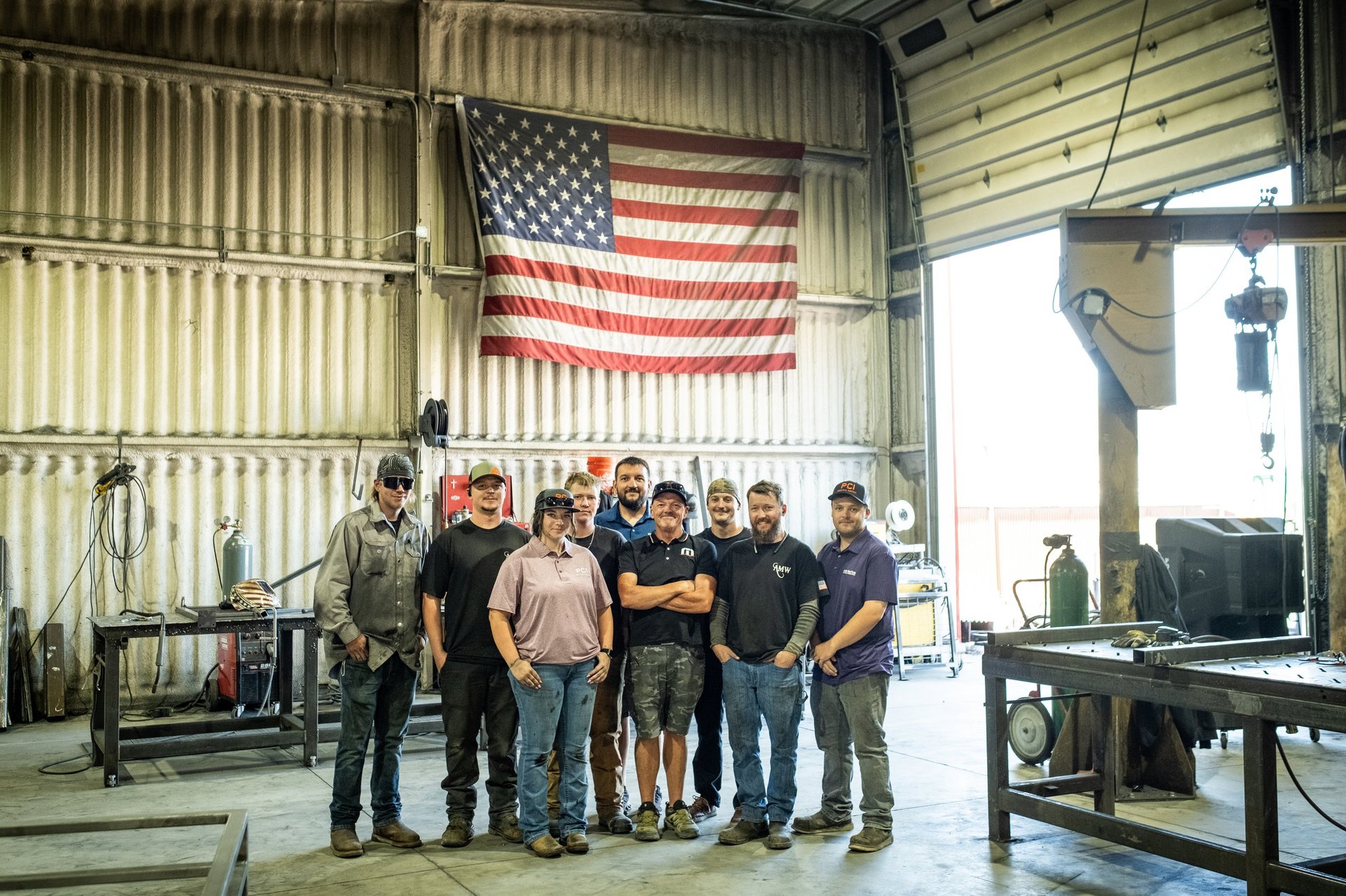 Group of workers standing together in an industrial warehouse with American flag on corrugated metal wall