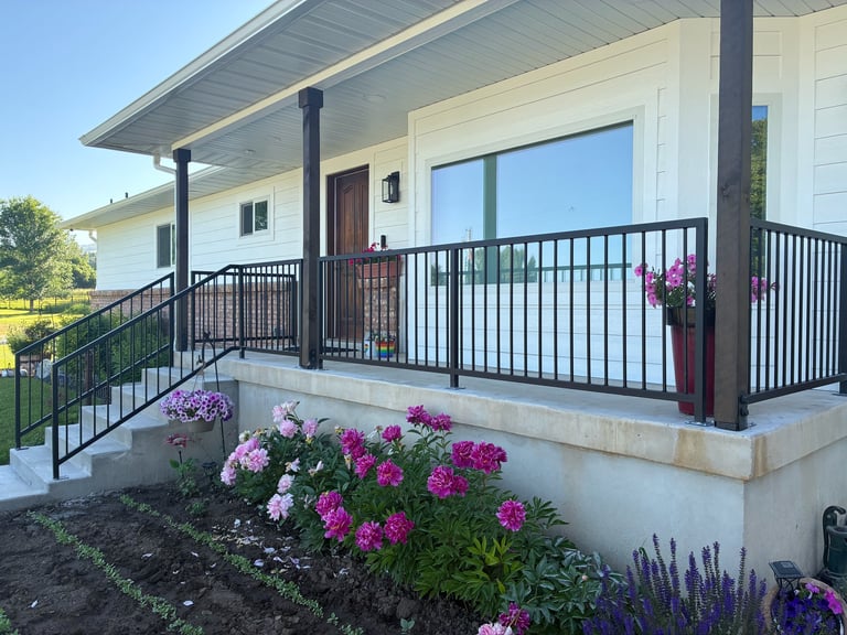 Modern house with white exterior, black metal railing on elevated deck, pink and purple flowers in front garden landscaping