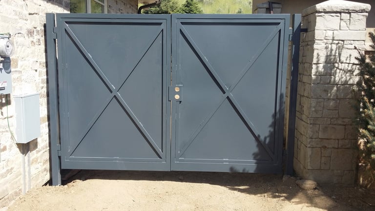 Pair of blue metal double gates with X-pattern bracing mounted between brick pillars at a property entrance