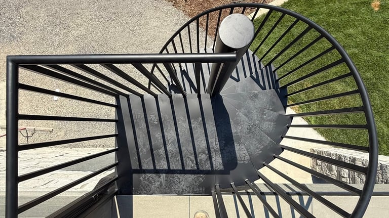 Overhead view of a black spiral staircase casting shadows on concrete and grass