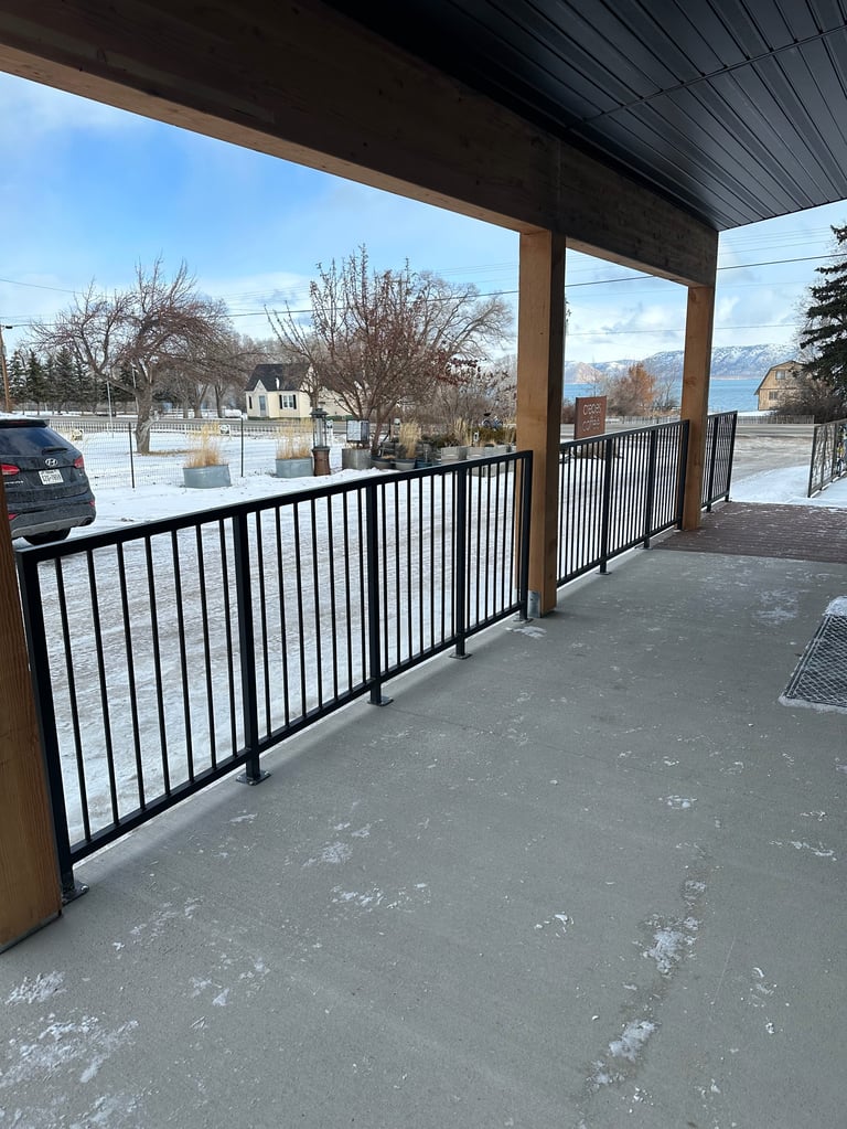 Covered patio with white and black metal railing overlooking snowy landscape and mountains in distance