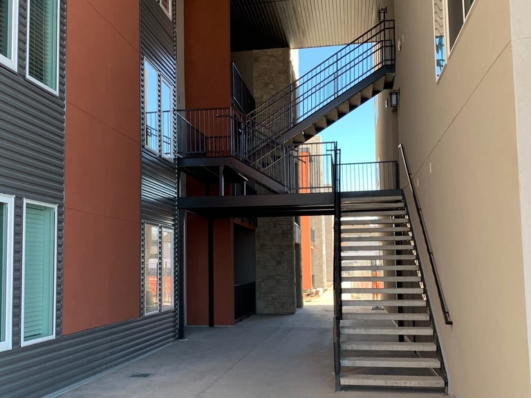 Modern multi-story building courtyard with metal stairs, ramps, and walkways connecting different levels, showing contemporary architecture