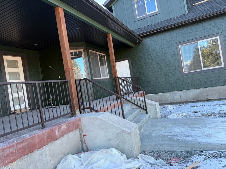 Modern house entrance with covered porch, black metal railing, wooden columns, and snow on the ground during winter.