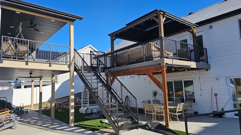 Modern two-story elevated deck with metal railings and wooden support beams attached to a white house under clear blue sky
