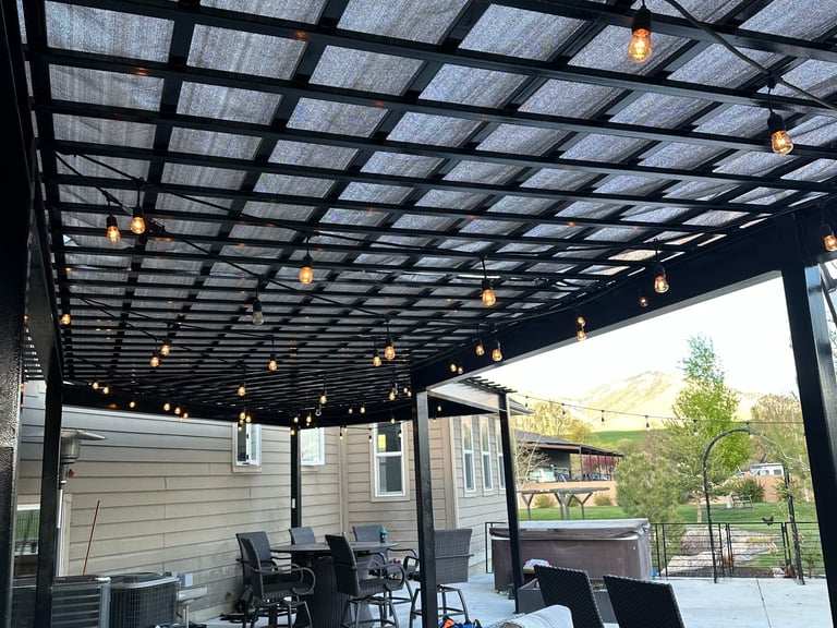 Modern covered patio with black metal pergola, hanging lights, furniture, and view of house and backyard